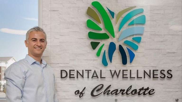 Dr. Sergei Shirman, DMD standing next to the Dental Wellness of Charlotte sign